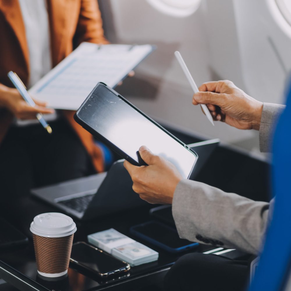 business people at meeting in private plane, Asian businessman in suit is talking to woman in jet and pointing at blank laptop screen, colleagues are discussing deal and flying in plane